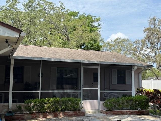 view of front of property with a sunroom, roof with shingles, and fence