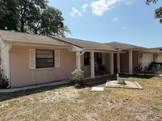 rear view of house featuring stucco siding, an attached garage, and a lawn