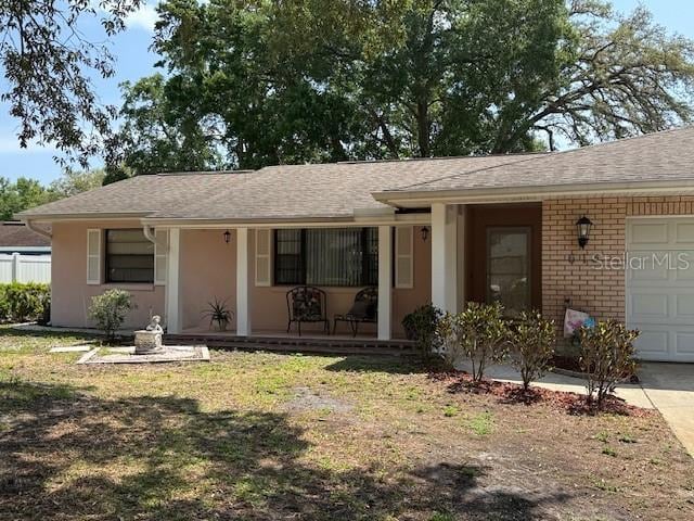 ranch-style house with a garage, a porch, driveway, brick siding, and roof with shingles