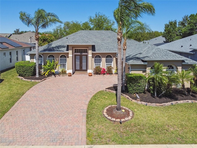 view of front of house featuring decorative driveway, stucco siding, french doors, and roof with shingles