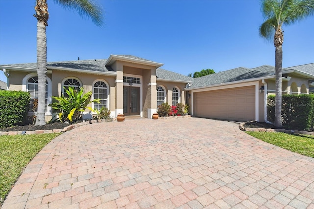view of front of house featuring stucco siding, a garage, french doors, and decorative driveway