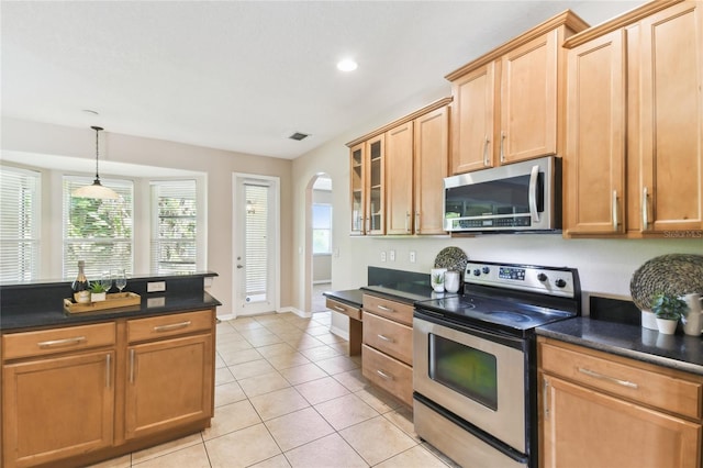 kitchen with stainless steel appliances, dark countertops, arched walkways, glass insert cabinets, and light tile patterned floors