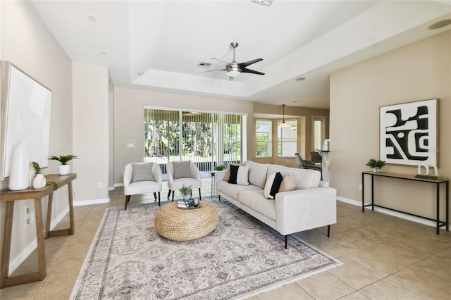 living area featuring light tile patterned flooring, a tray ceiling, visible vents, and a ceiling fan