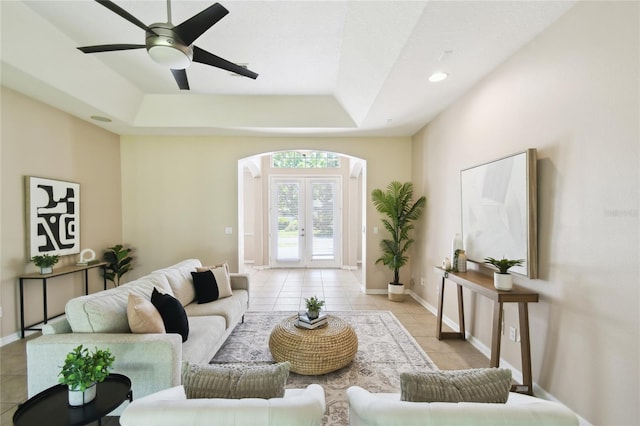 living room featuring arched walkways, a tray ceiling, french doors, and light tile patterned floors