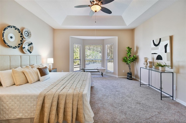 carpeted bedroom with a tray ceiling, baseboards, and ceiling fan