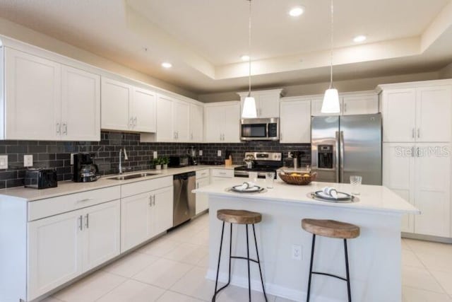 kitchen featuring white cabinetry, stainless steel appliances, a tray ceiling, and a sink