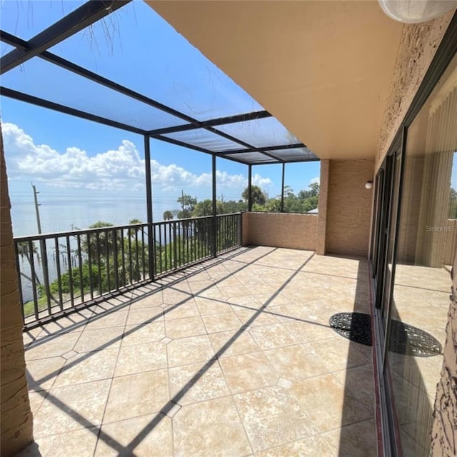 view of patio / terrace featuring glass enclosure, a water view, and a balcony
