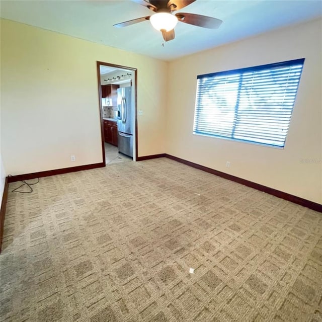 spare room with a ceiling fan, baseboards, and light carpet