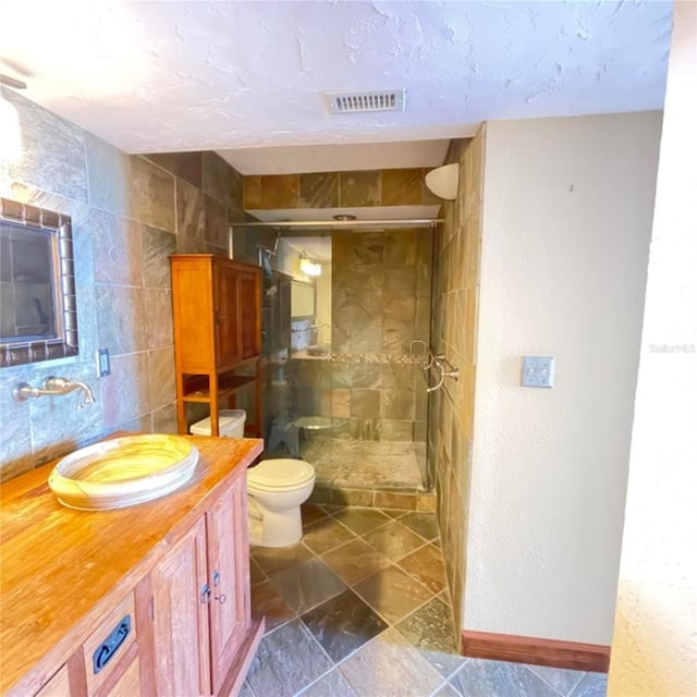 bathroom with visible vents, toilet, vanity, a stall shower, and tile walls