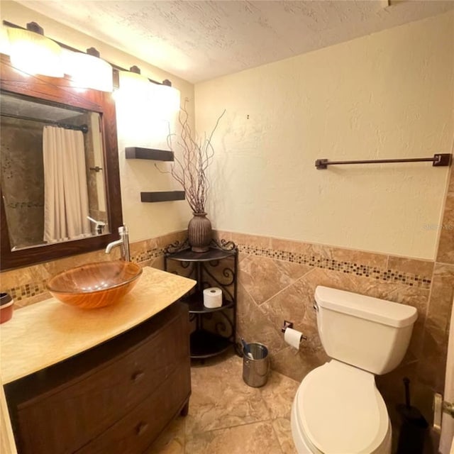 full bath featuring curtained shower, a wainscoted wall, toilet, vanity, and a textured ceiling