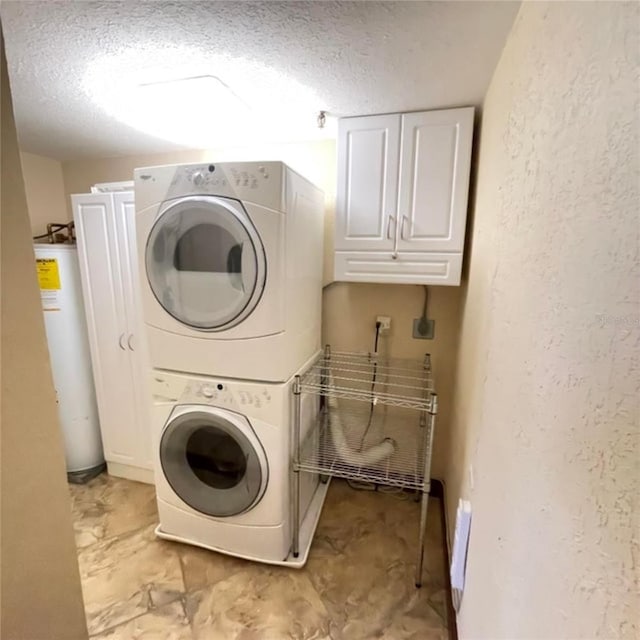 laundry room featuring a textured ceiling, water heater, stacked washing maching and dryer, cabinet space, and a textured wall