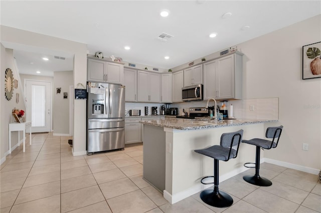 11038 Leafshore Loop, Orlando, FL 32829 - kitchen with appliances with stainless steel finishes, gray cabinets, a peninsula, a breakfast bar area, and light stone counters