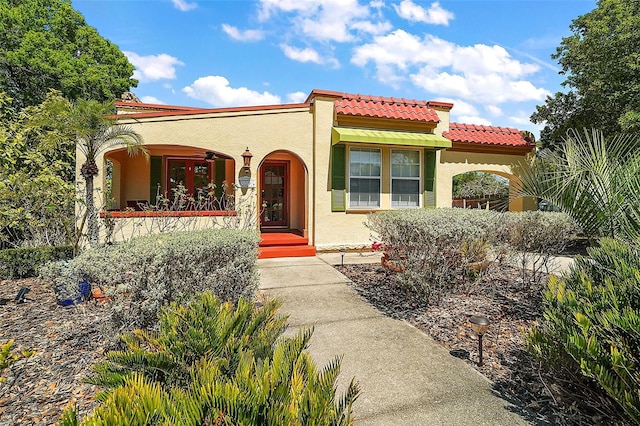 mediterranean / spanish home featuring stucco siding, covered porch, and a tiled roof