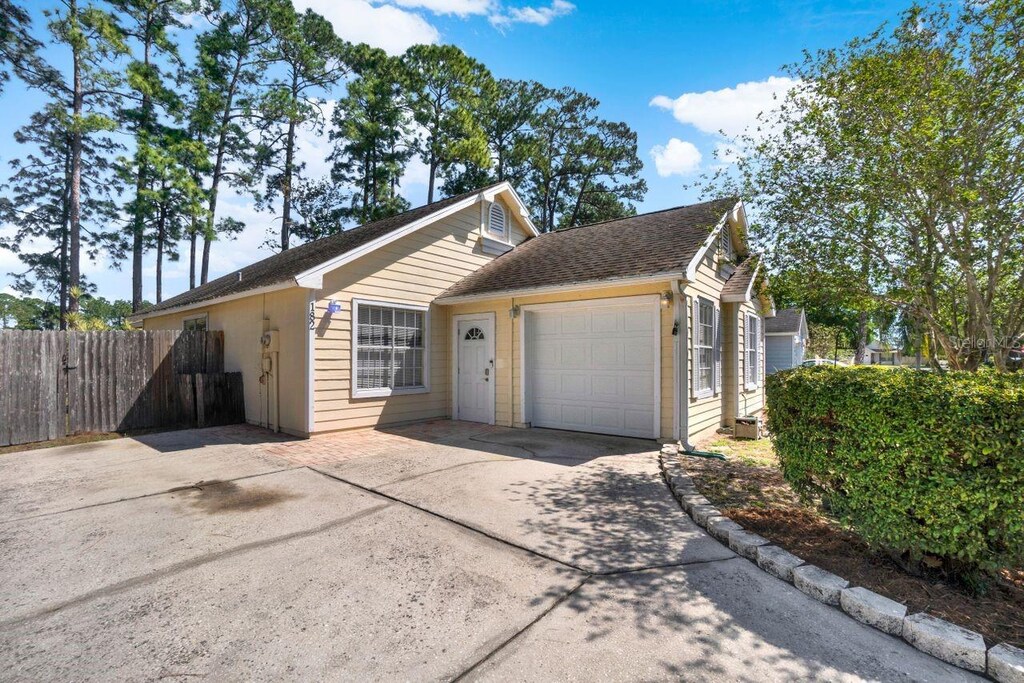 ranch-style house featuring a garage, fence, concrete driveway, and roof with shingles
