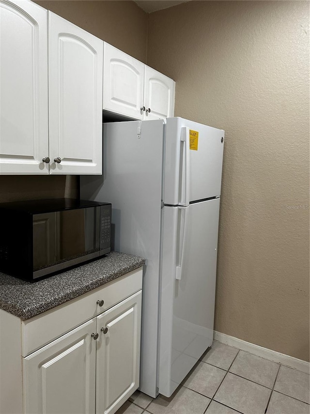 860 N Orange Ave Unit 149, Orlando, FL 32801 - kitchen featuring black microwave, light tile patterned floors, white cabinetry, dark stone counters, and freestanding refrigerator