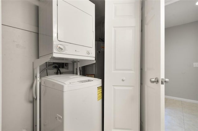 clothes washing area featuring baseboards, laundry area, stacked washer and dryer, and light tile patterned flooring