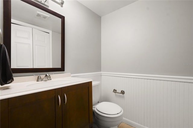 half bath featuring vanity, wainscoting, toilet, and visible vents