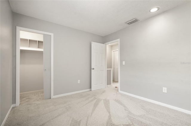 unfurnished bedroom featuring a walk in closet, visible vents, baseboards, carpet flooring, and recessed lighting