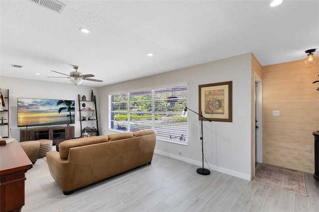 living area with wooden walls, a ceiling fan, visible vents, light wood-style flooring, and a textured ceiling