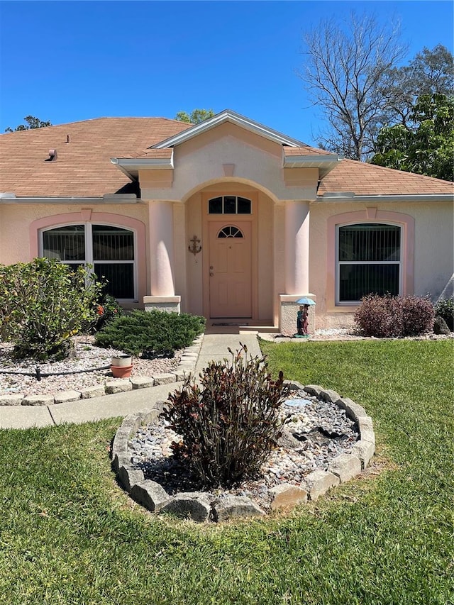 property entrance with a shingled roof, a yard, and stucco siding