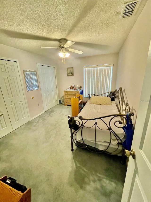 bedroom with a textured ceiling, multiple closets, visible vents, and carpet