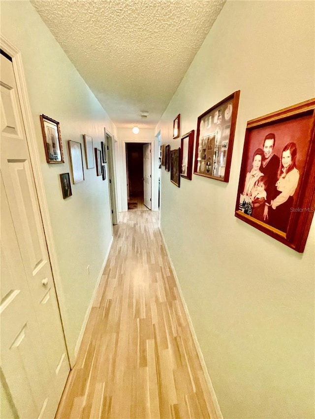 hallway with light wood finished floors, a textured ceiling, and baseboards