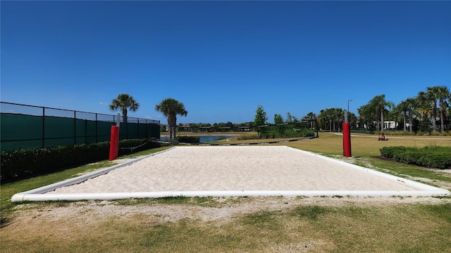 view of community featuring volleyball court, fence, a water view, and a yard
