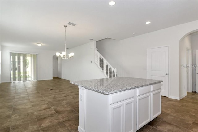kitchen featuring white cabinets, arched walkways, a center island, and visible vents
