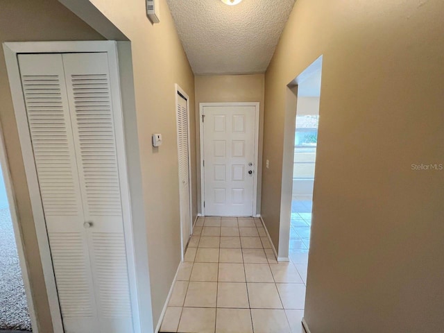 corridor featuring light tile patterned flooring, a textured ceiling, and baseboards