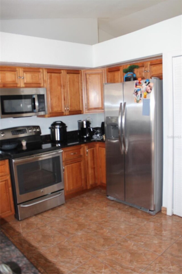855 San Pedro Ct, Kissimmee, FL 34758 - kitchen featuring light tile patterned flooring, vaulted ceiling, brown cabinets, stainless steel appliances, and dark countertops