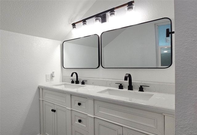 full bath featuring double vanity, lofted ceiling, a textured wall, and a sink