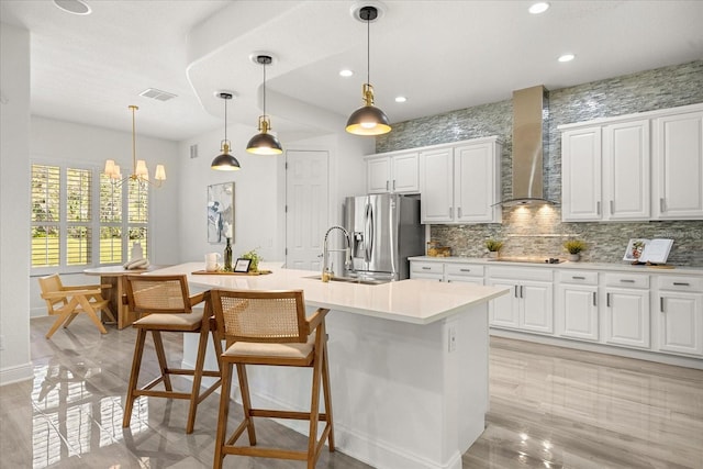 kitchen featuring visible vents, a sink, stainless steel refrigerator with ice dispenser, black electric stovetop, and wall chimney exhaust hood
