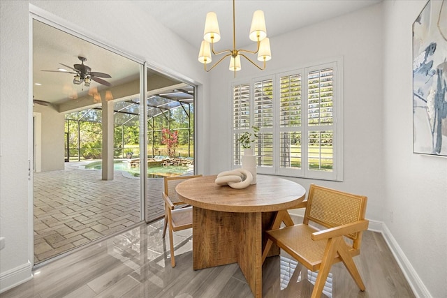 dining area featuring ceiling fan with notable chandelier, baseboards, and wood finished floors