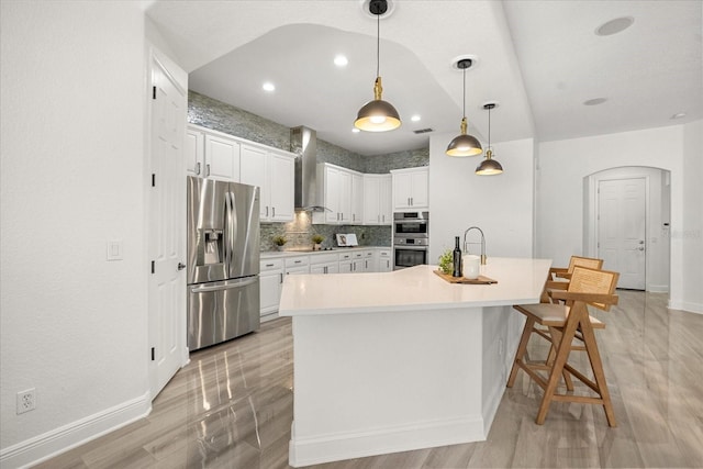 kitchen featuring a sink, stainless steel appliances, white cabinets, wall chimney exhaust hood, and tasteful backsplash