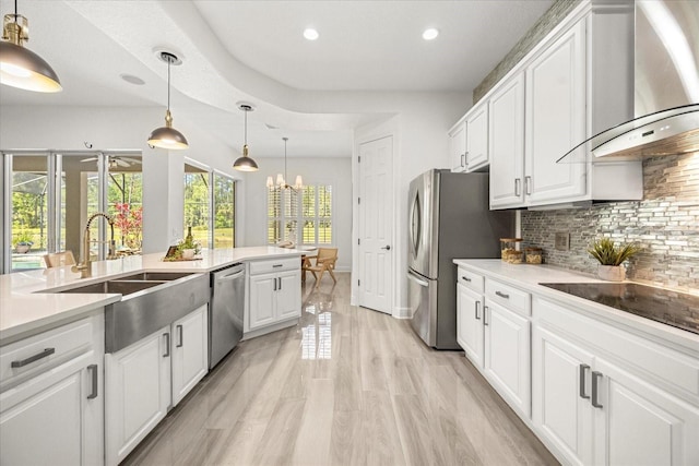 kitchen featuring backsplash, wall chimney range hood, appliances with stainless steel finishes, white cabinets, and a sink