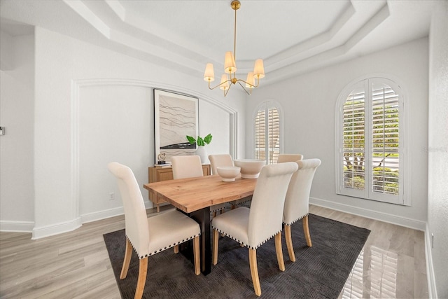 dining area with a notable chandelier, light wood-style flooring, a raised ceiling, and baseboards