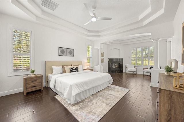 bedroom with a raised ceiling, visible vents, and ornate columns