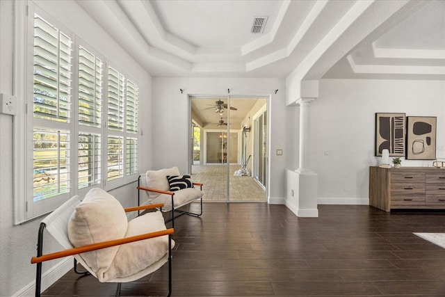 living area featuring a ceiling fan, wood finished floors, visible vents, ornate columns, and a raised ceiling