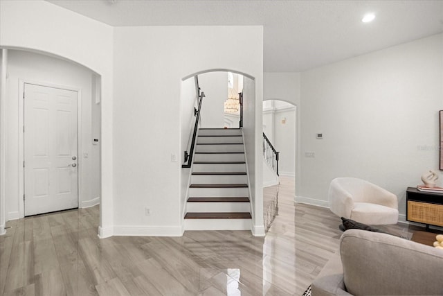 staircase featuring recessed lighting, baseboards, arched walkways, and wood finished floors