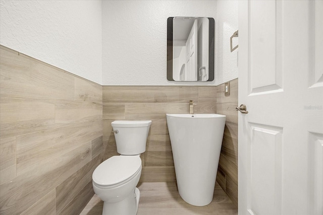 half bath with toilet, tile walls, and a textured wall