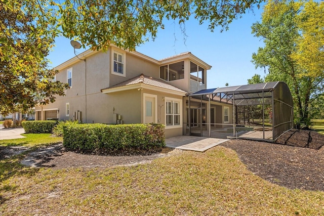 back of house with a lanai, a tiled roof, stucco siding, a yard, and a patio area
