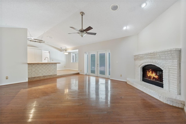 unfurnished living room featuring a ceiling fan, a fireplace, vaulted ceiling, a sink, and wood-type flooring