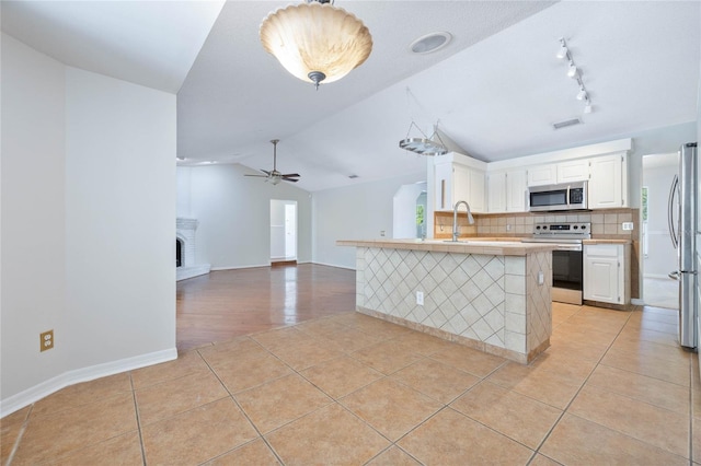 kitchen with ceiling fan, vaulted ceiling, light countertops, stainless steel appliances, and light tile patterned flooring