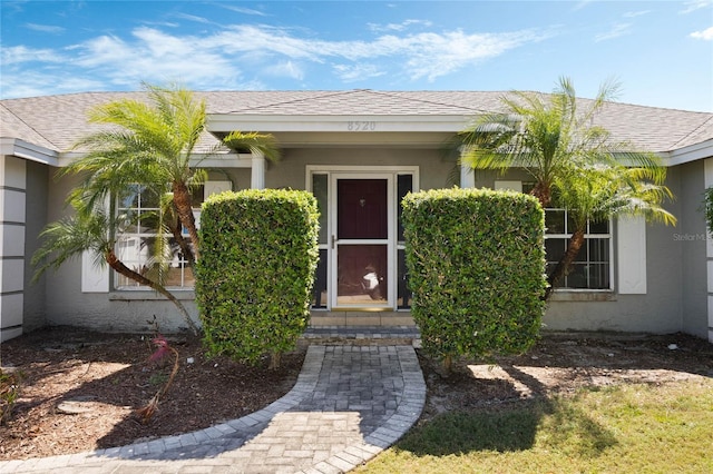 view of exterior entry featuring roof with shingles and stucco siding