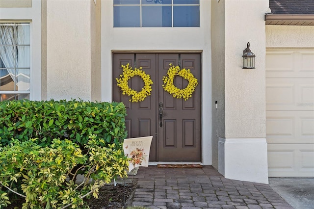 view of exterior entry featuring a garage and stucco siding