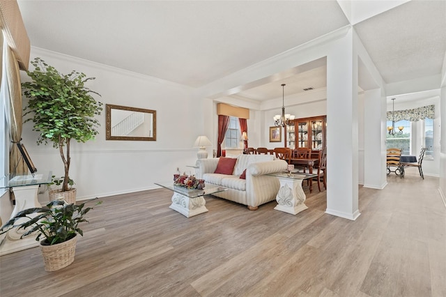 living room with crown molding, baseboards, light wood finished floors, and a chandelier