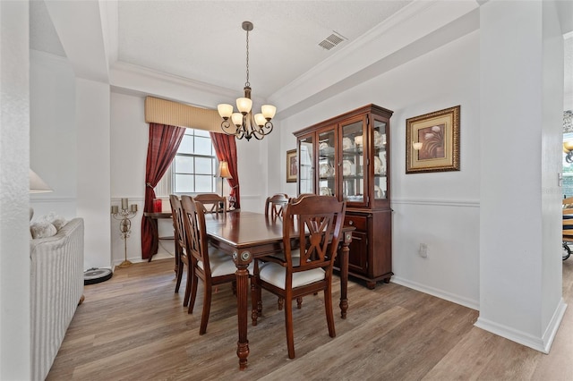dining room featuring baseboards, an inviting chandelier, ornamental molding, visible vents, and wood finished floors