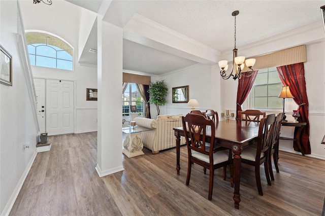 dining room featuring a chandelier, baseboards, crown molding, and wood finished floors