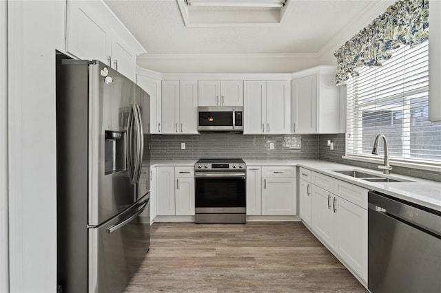 kitchen featuring tasteful backsplash, light countertops, white cabinetry, stainless steel appliances, and a sink