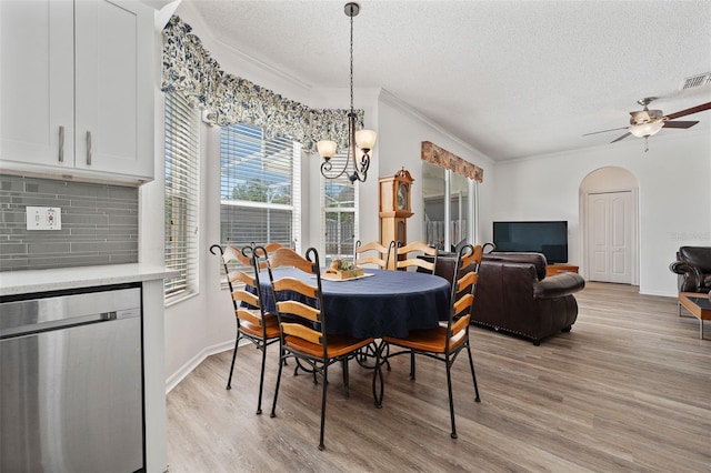 dining room featuring light wood-style floors, ceiling fan with notable chandelier, arched walkways, a textured ceiling, and ornamental molding